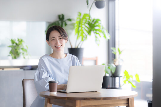観葉植物のあるオシャレな明るいオフィスでノートパソコンで仕事をする日本人女性 オフィスワーク・ビジネスシーン　カメラ目線