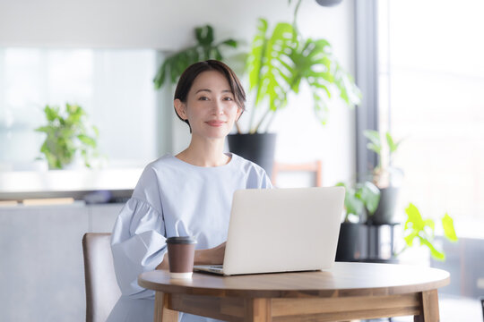 観葉植物のあるオシャレな明るいオフィスでノートパソコンで仕事をする日本人女性 オフィスワーク・ビジネスシーン　カメラ目線