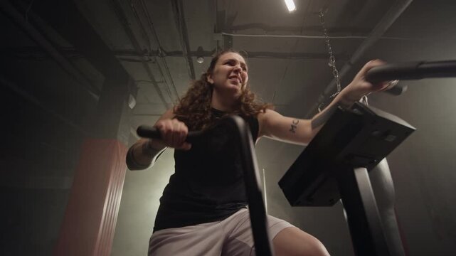 Young Caucasian woman training intensely on air bike in gym. Footage is perfect for fitness brand advertisements, gym promotions, and motivational cardio workout campaigns