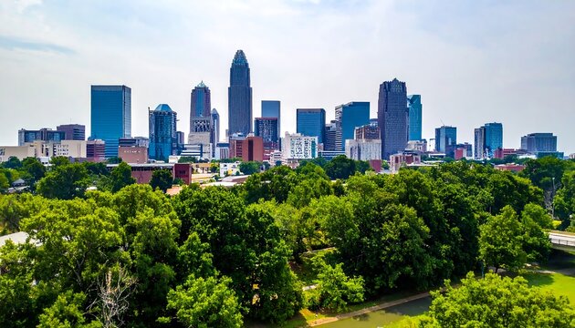 Aerial view of a city skyline with tall buildings, set against a bright sky, lush green trees