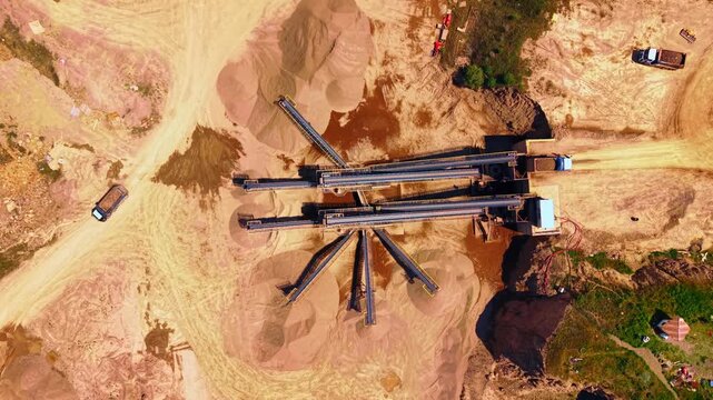 Overhead aerial view of aggregate processing facility and conveyors. Straight down perspective showing sorting machinery, sand mounds, dirt roads and sunny daylight.