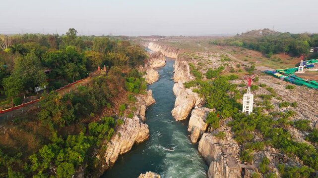 Smooth forward-moving 4K drone shot following the Narmada River through the marble gorge at Dhuandhar Waterfall, Bhedaghat, Jabalpur, Madhya Pradesh, India, captured in early morning natural light.