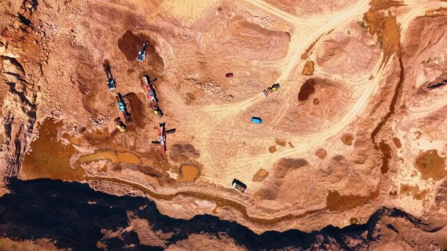 Aerial view of industrial stone quarry and dirt roads. Construction machinery and transport vehicles work on dry brown soil near deep shadow.