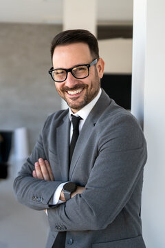 Young happy successful businessman with arms crossed smiling at corporate office
