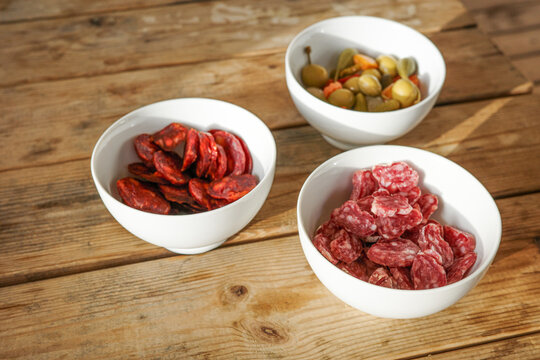 Spanish tapas with chorizo, fuet and olives in white bowls