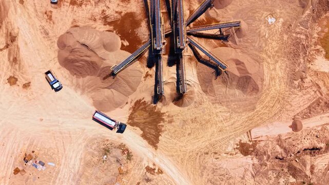 Aerial view of a sand quarry with processing machinery. Top down shot of sand mounds, conveyor belts and trucks on ground.
