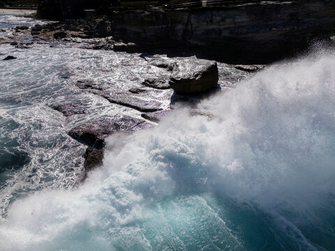 Powerful ocean wave breaks over rock platform in dramatic light from aerial view. Location is Ben Buckler headland at Bondi Beach in Sydney, Australia