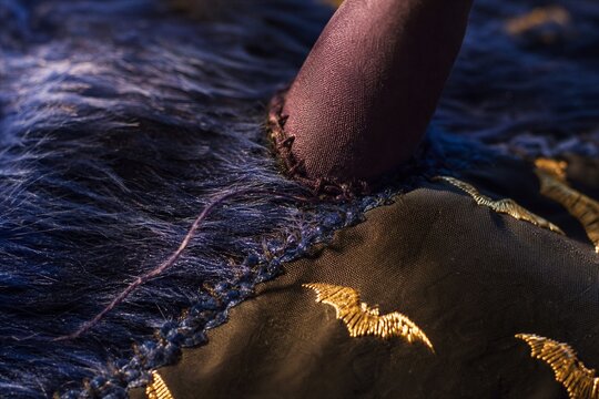 Close-up of a handmade Halloween costume with faux fur, a horn, and metallic bat embroidery on dark fabric