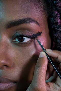 Close up of woman applying black bat wing eyeliner detail with brush. Halloween makeup inspiration. Creative beauty look with colorful eyeshadow. portrait format