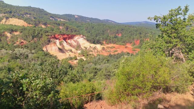 Distant view of colorful layered rock cliffs in the Colorado Provencal, a spectacular semi-natural landscape of ancient ochre quarries located next to the village of Rustrel , France.