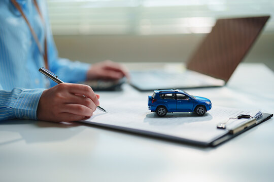 Close-up customer signing a car insurance or vehicle financing agreement beside a model SUV, auto insurance, vehicle ownership, loan approval, leasing, and financial protection