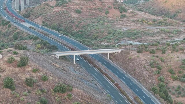 Distant drone view of a regional multi-lane highway crossing dry hills and rugged countryside landscape with bridge infrastructure, Malaga, Andalusia, Spain