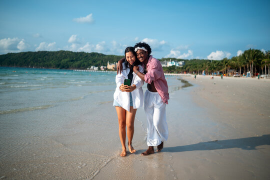Trendy digital creator couple taking selfie by the beach, sharing travel content for social media