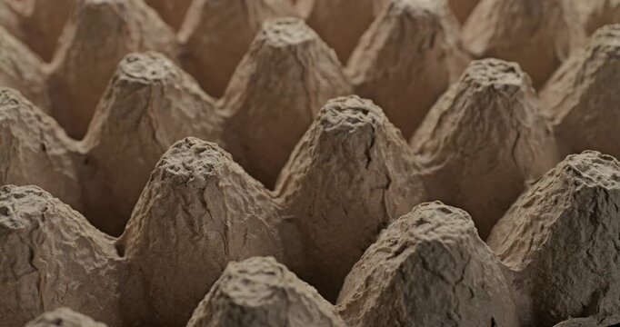 Recycled paper. Close-up of empty beige molded pulp tray with rough fibrous surface and conical cells. Smooth continuous rotation shows subtle light and shadow shifts across the eco recycled texture.	