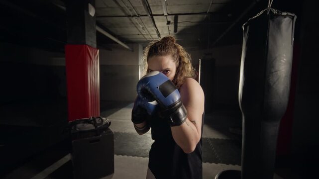 Portrait of young Caucasian woman wearing boxing gloves, throwing punches directly at camera in slow motion. Footage is perfect for female empowerment and sports marketing campaigns