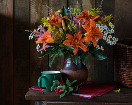 Colorful bouquet with orange daylilies, feverfew daisies and garden flowers in rustic clay vase on wooden table against dark wooden background. Cozy country still life, summer farmhouse decor