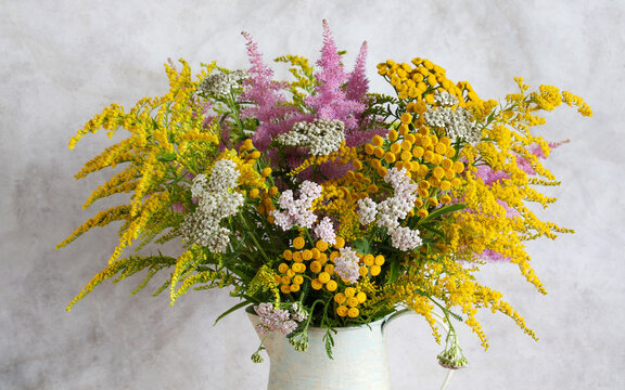 summer bouquet of tansy, yarrow, goldenrod and astilbe arranged in a ceramic pitcher against a neutral backdrop
