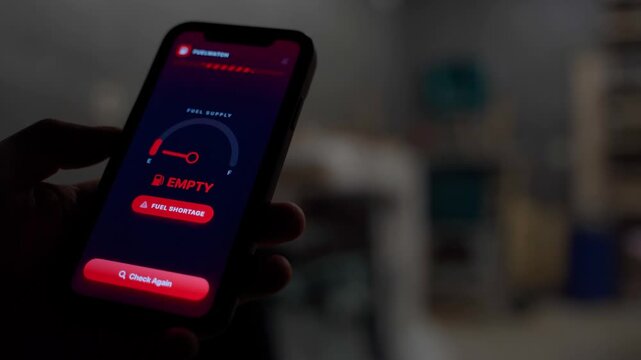 Hand holding smartphone with fuel monitoring app showing empty tank and fuel shortage warning 