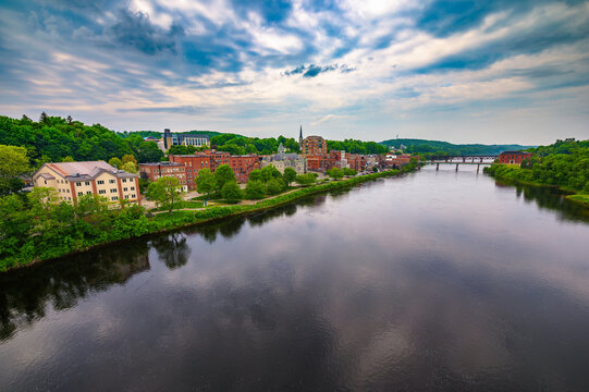 Downtown Augusta, Maine, from Memorial Bridge, with the Kennebec River reflecting brick buildings, lush green hills, and dramatic clouds.