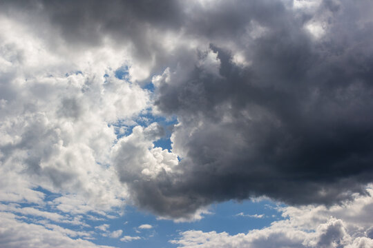Dramatic dark storm clouds gathering in the sky creating a moody atmospheric contrast with patches of bright blue light piercing through the heavy textured weather formations above
