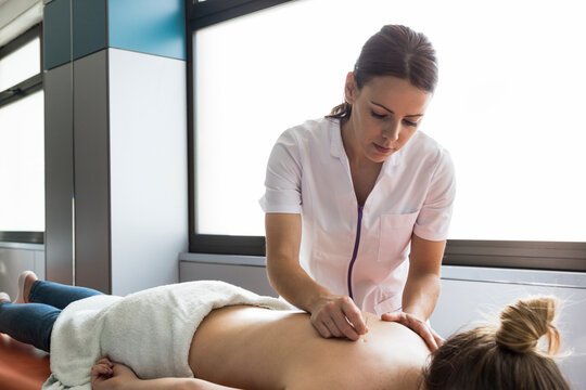 Close up acupuncturist applying acupuncture needles to woman?s back