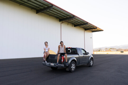 Two acrobats sitting on car bonnet, taking a break