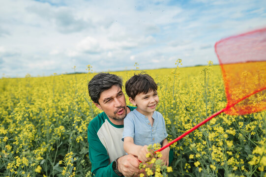 Father and son with a butterfly net in a summer rapeseed field