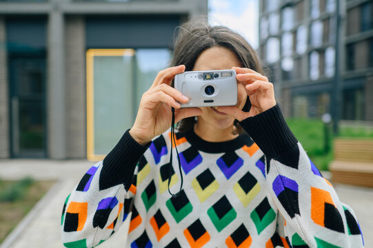 Woman in a colorful sweater holds a retro camera outdoors
