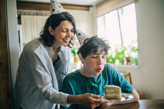 Mother holds cake while teenage son blows out birthday candle