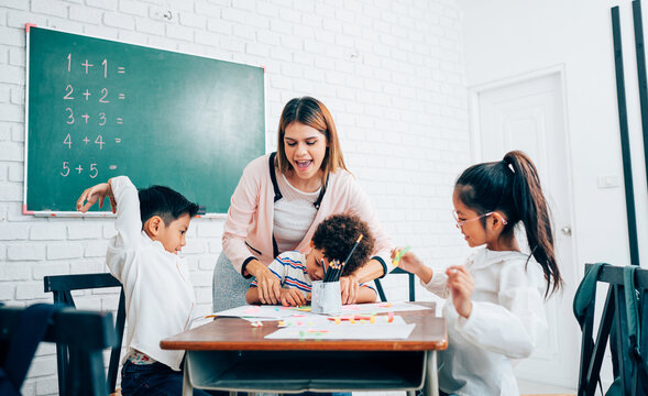 Happy school teacher and students having interesting engaging activities in class. Little children sitting around classroom table, talking and playing fun games together