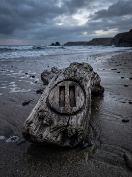 Weathered driftwood with pause symbol carved on a moody beach.