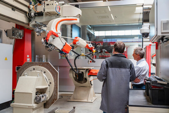 Male employees inspect an industrial robot in a factory