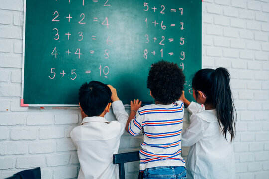 Happy school teacher and students having interesting engaging activities in class. Little children sitting around classroom table, talking and playing fun games together
