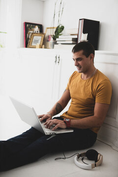 Smiling young man sitting on the floor using laptop