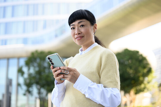 Smiling woman using smartphone outdoors in urban casual setting