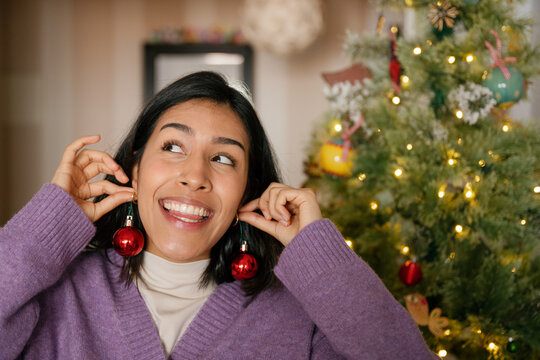 Young woman holding red Christmas ornaments like earrings at home