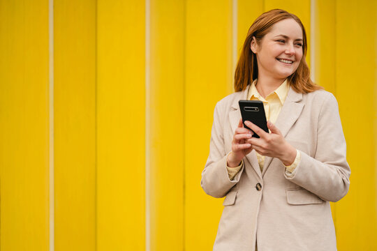 Smiling businesswoman holding smartphone against yellow background