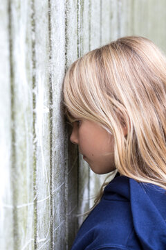 Profile of sad blond girl leaning against wooden wall