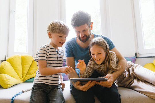 Son and daughter using tablet PC with father at home