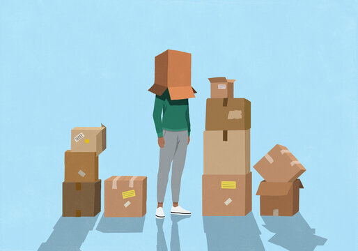 Woman surrounded by moving boxes standing with cardboard box covering head against blue background