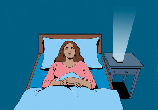 Smart phone screen emitting bright light on bedside table next to worried woman laying awake in bed 