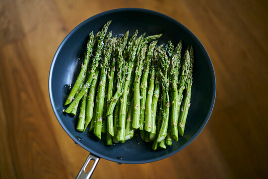 View from above of vibrant green asparagus spears cooking in skillet with sea salt flakes