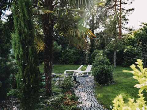 White lounge chairs in a lush green luxury garden by a pool