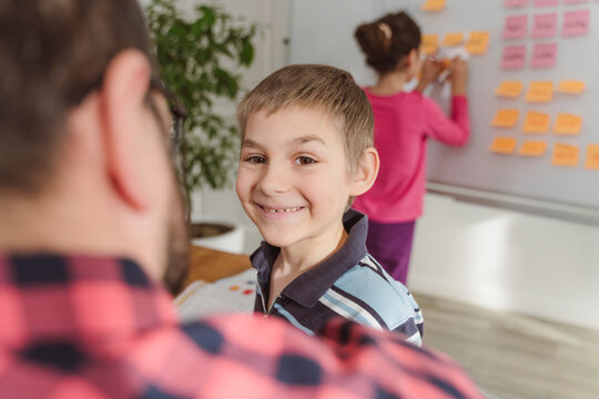 Smiling boy by teacher with sister writing on whiteboard in background