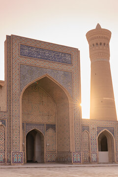 Kalyan Mosque and Kalyan Minaret at sunset in Bukhara, Uzbekistan. Ornate iwan with blue tilework and Arabic calligraphy glows in golden light. Ideal for travel guides, cultural publications.