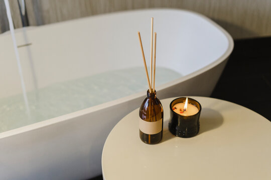 Incense sticks by burning scented candle on table near bathtub
