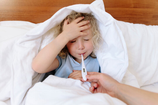 Mother taking care of sick daughter and using thermometer on bed