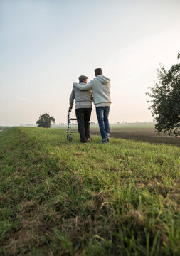 Senior man and grandson in rural landscape with wheeled walker