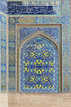 Ornate tilework on the facade of Nadir Divan Begi Madrasah in Bukhara, Uzbekistan. Blue and yellow floral arabesques fill a pointed arch niche framed by calligraphy and geometric patterns.