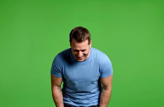 Man in blue t-shirt bending over and laughing on a green background.
